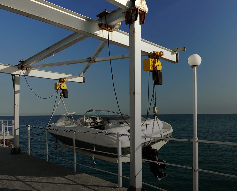 Boat hoisted on dock crane over water.
